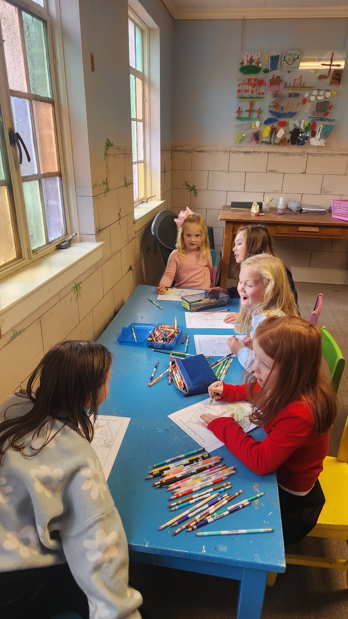Girls working on coloring sheets around the Sunday School table