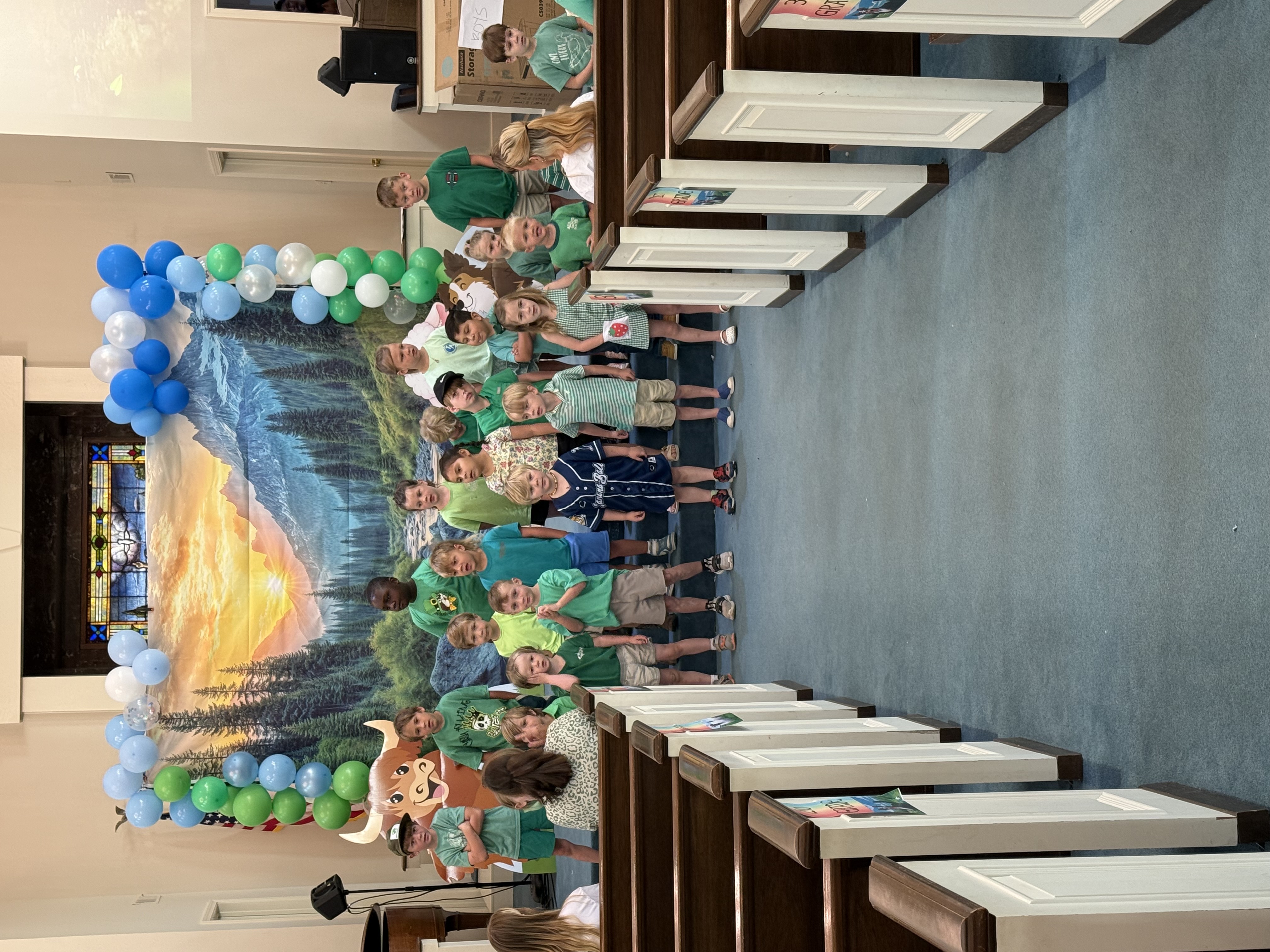 Children posing in front of the VBS backdrop with balloons